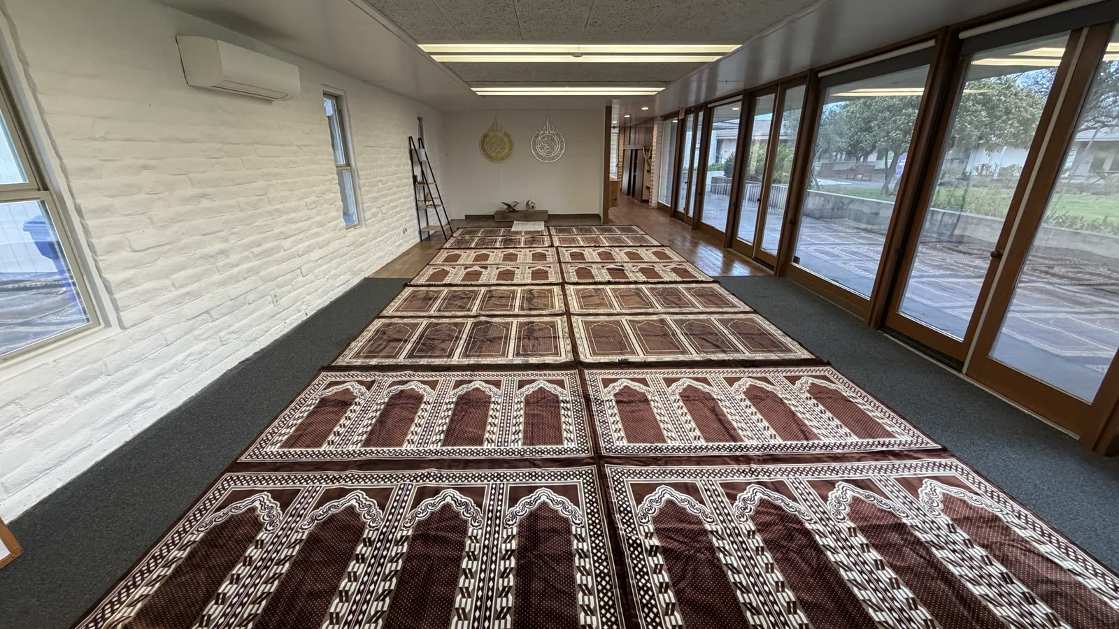 Prayer hall with rows of prayer rugs and windows along one side